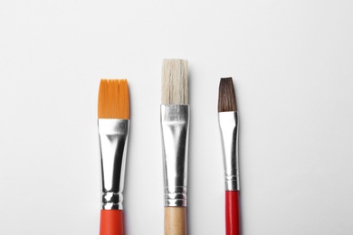 Different paint brushes on white background, top view