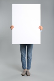 Photo of Woman holding white blank poster on grey background. Mockup for design