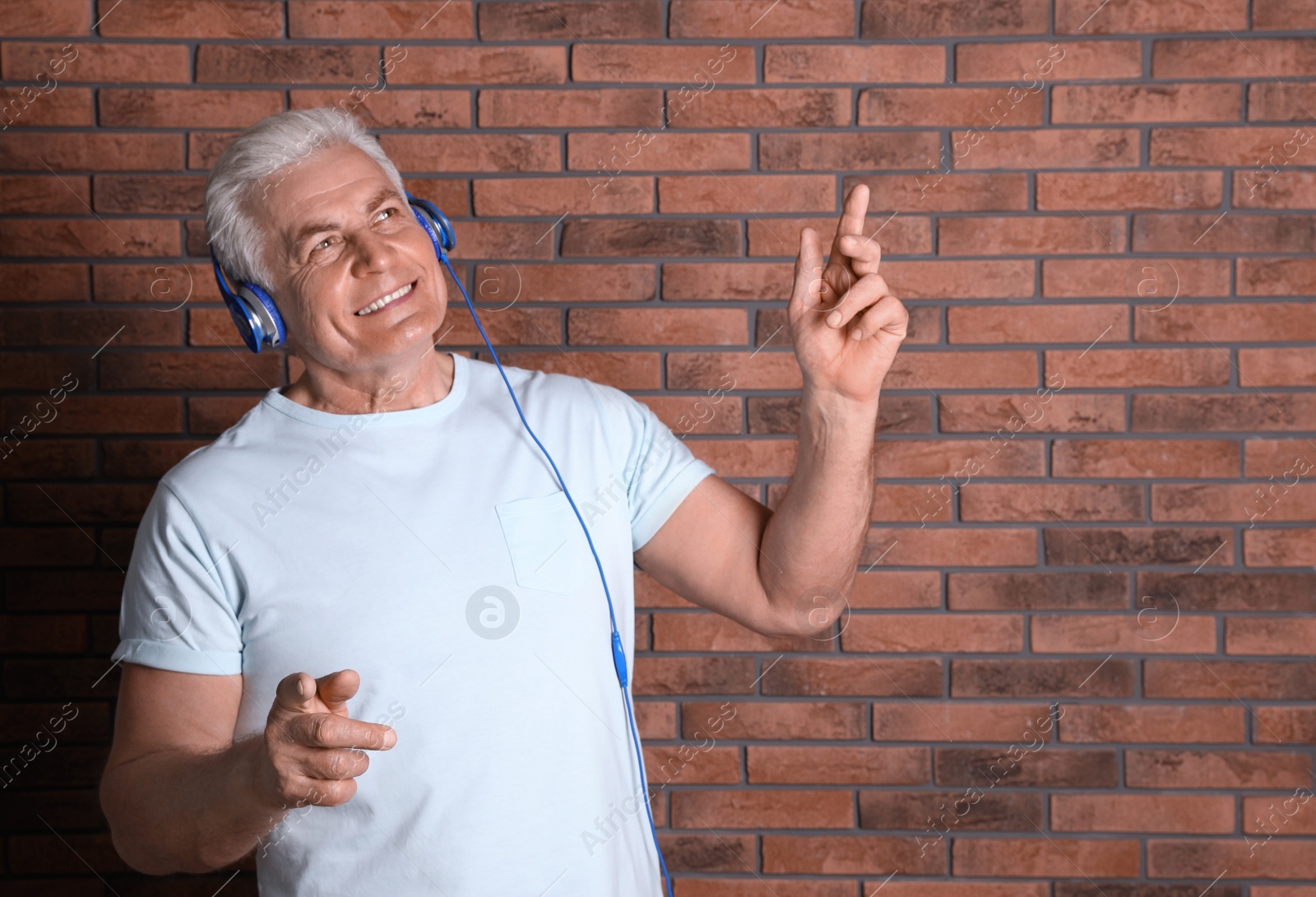 Photo of Mature man enjoying music in headphones against brick wall. Space for text