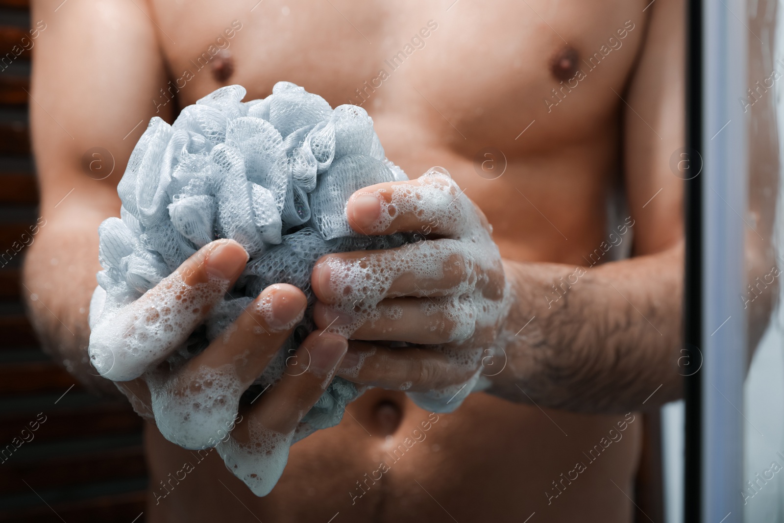 Photo of Man with mesh pouf taking shower at home, closeup