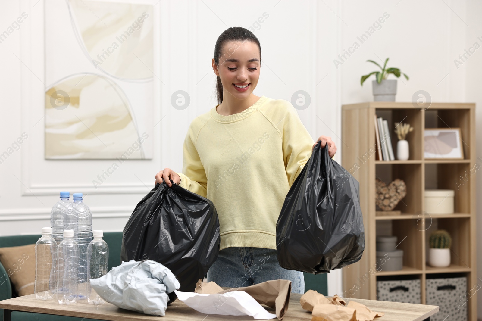 Photo of Smiling woman with plastic bags separating garbage in room