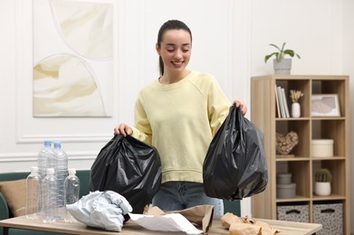 Photo of Smiling woman with plastic bags separating garbage in room