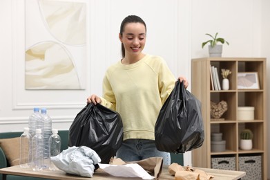 Smiling woman with plastic bags separating garbage in room