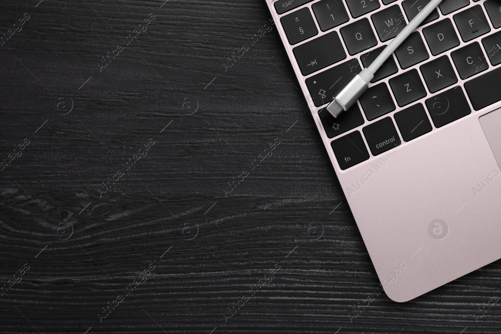 Photo of USB cable with type C connector and laptop on black wooden table, top view. Space for text