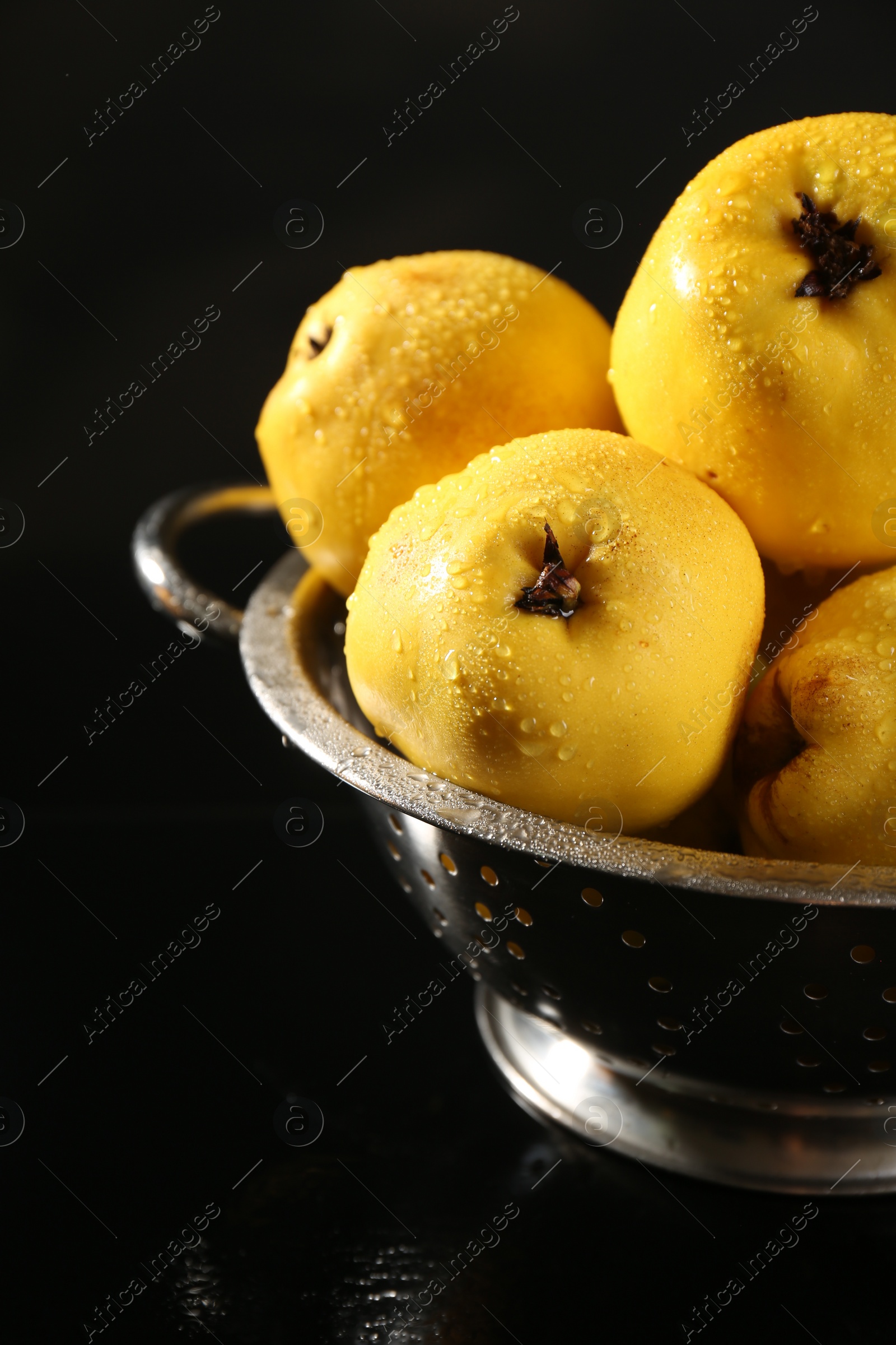 Photo of Tasty ripe quinces with water drops in metal colander on black background, closeup