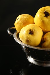 Photo of Tasty ripe quinces with water drops in metal colander on black background, closeup