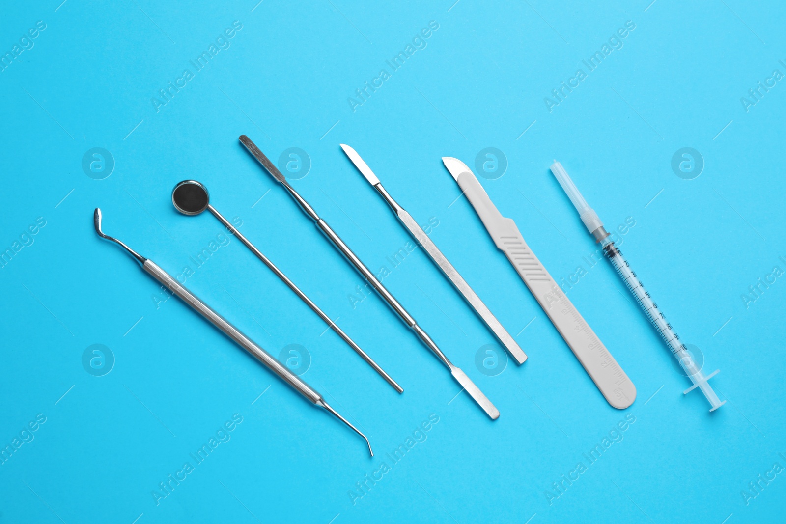 Photo of Set of different dentist's tools and syringe on light blue background, flat lay