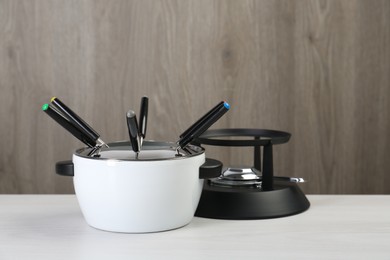 Photo of Fondue set on white wooden table, closeup