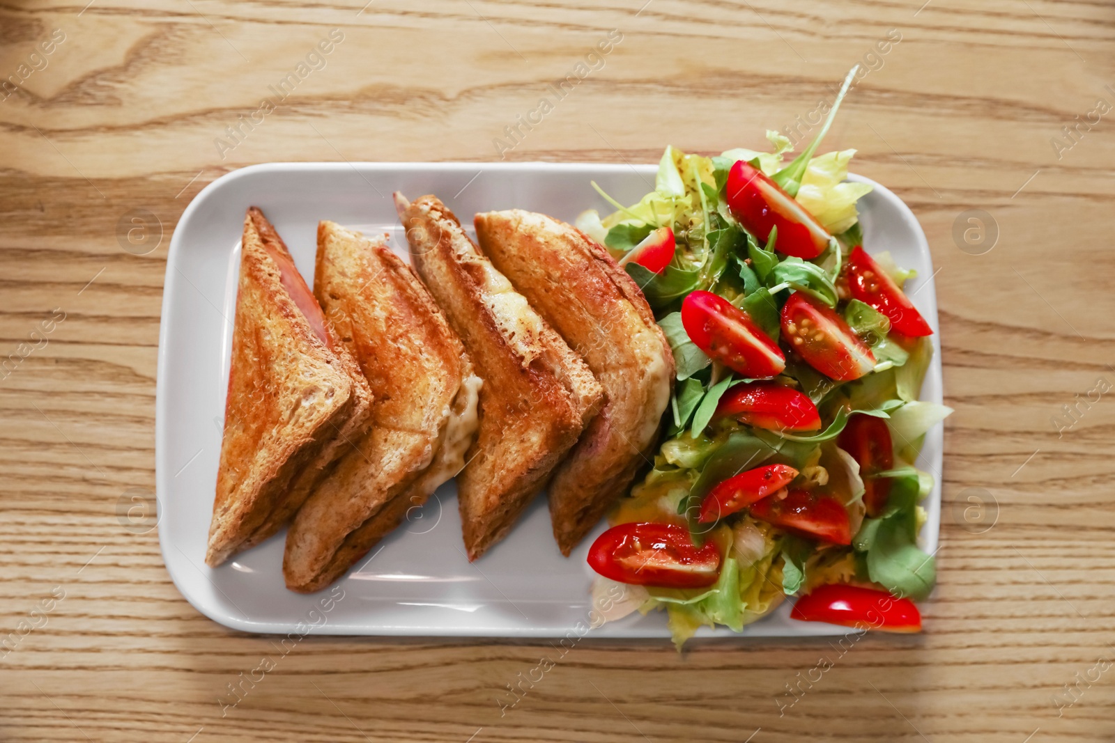 Photo of Plate of delicious toasts and salad on wooden table, top view