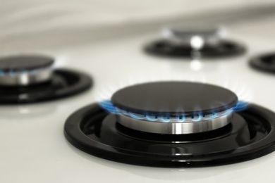 Photo of Gas burner with blue flame on modern stove, closeup