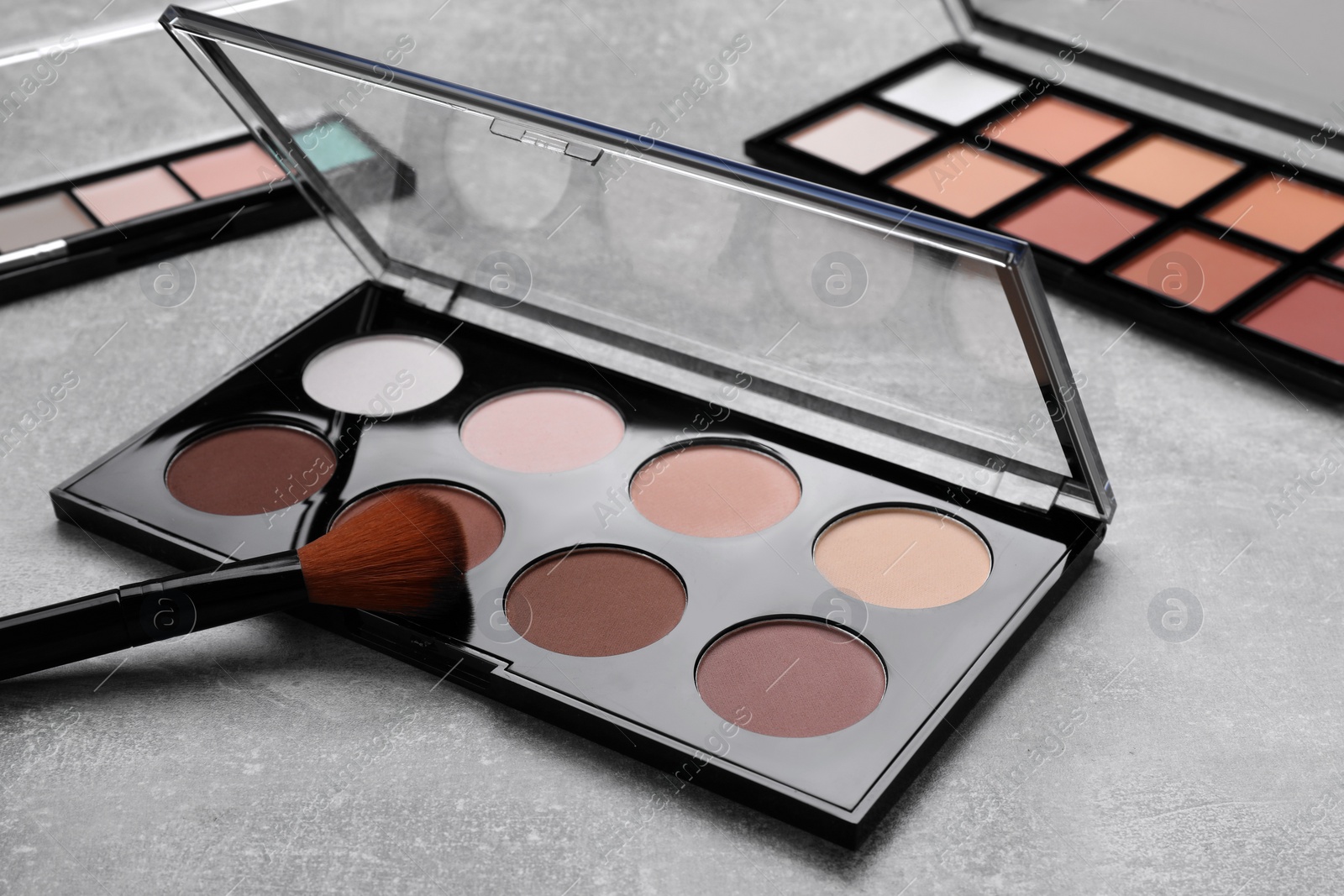 Photo of Contouring palettes and brush on light gray background, closeup. Professional cosmetic product