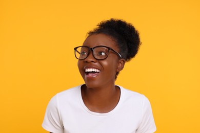 Portrait of happy young woman in eyeglasses on orange background