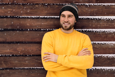 Photo of Young man wearing warm clothes near wooden wall.  Winter vacation