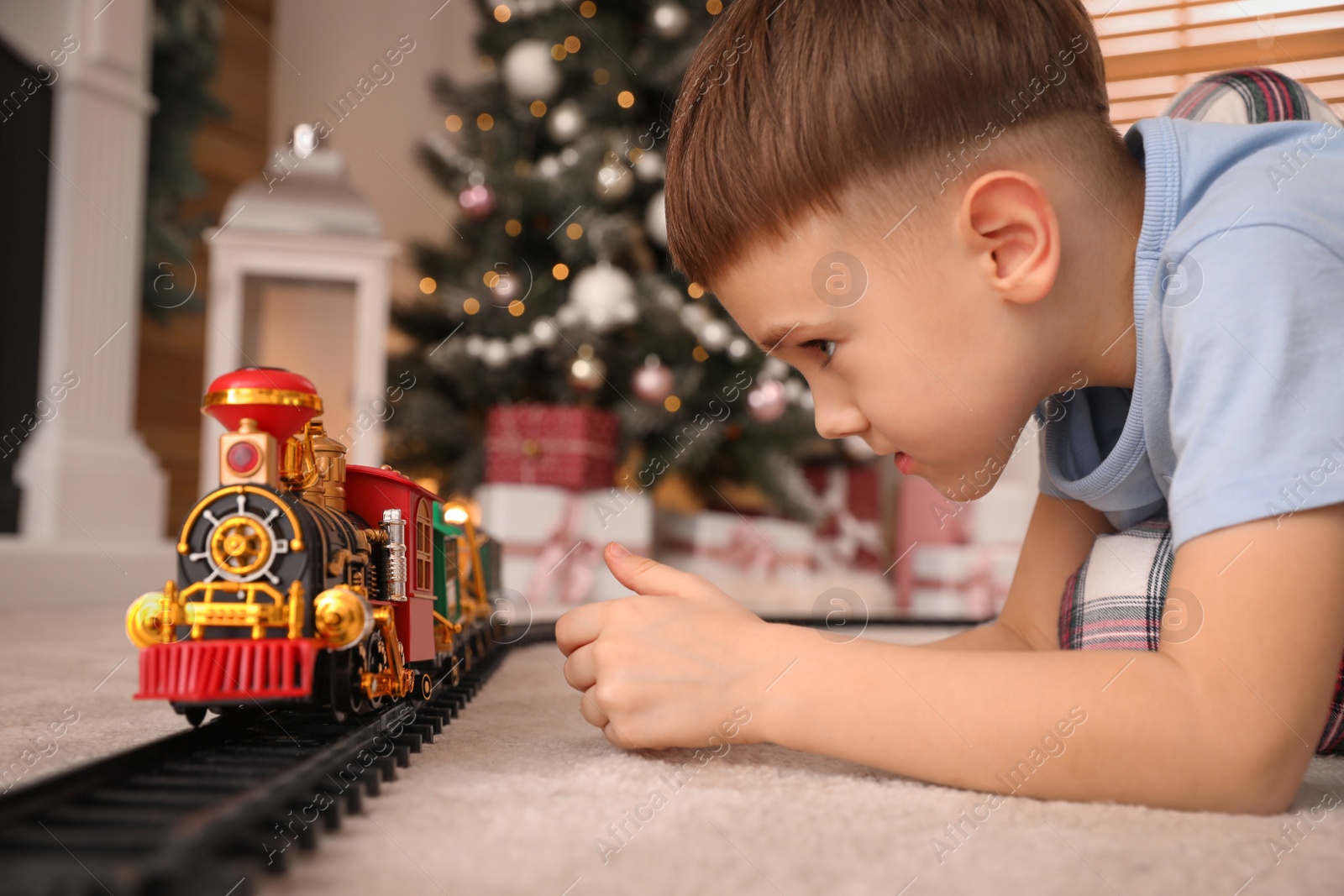 Photo of Little boy playing with colorful train toy in room decorated for Christmas