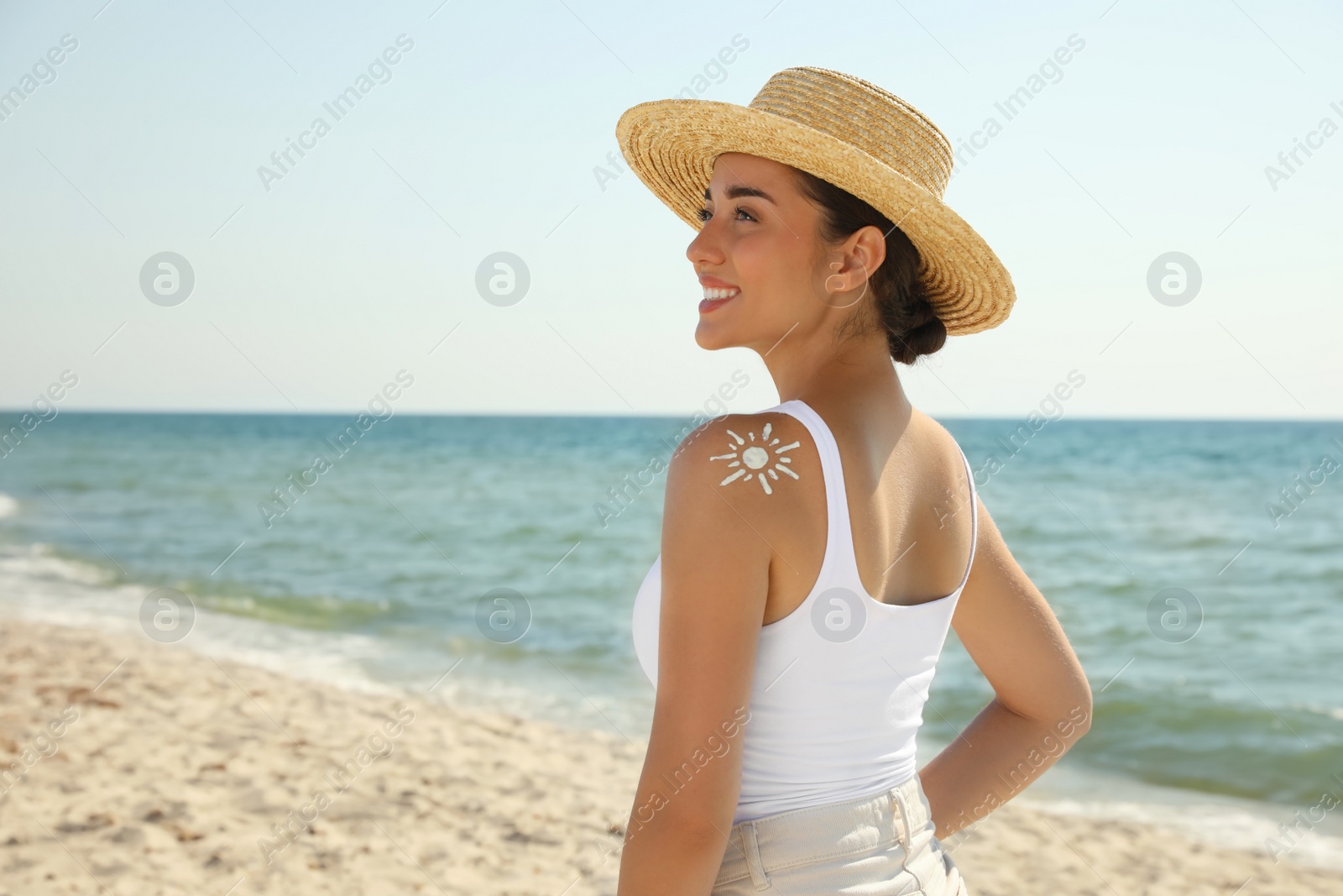 Photo of Beautiful young woman with sun protection cream on shoulder at beach