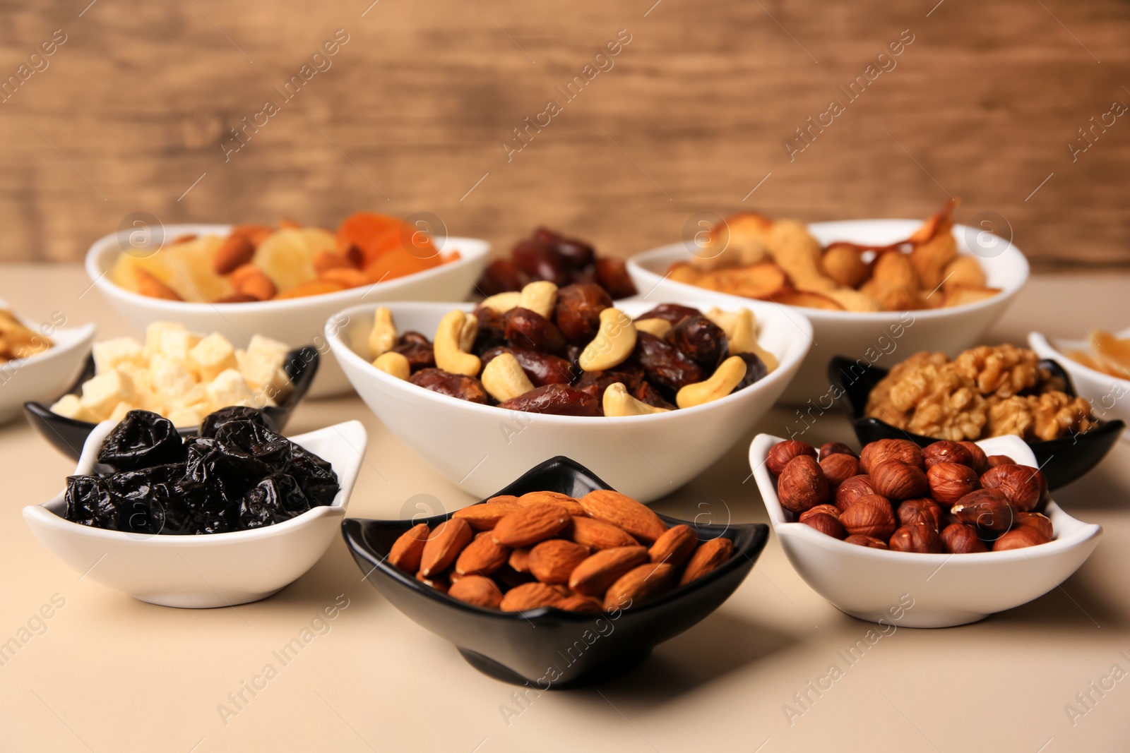 Photo of Bowls with dried fruits and nuts on beige background