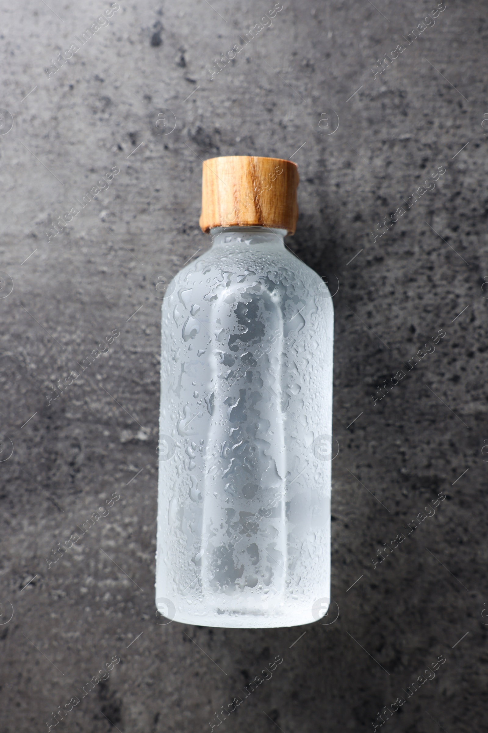 Photo of Bottle of cosmetic product on wet grey background, top view