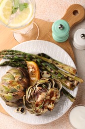 Tasty grilled artichokes and asparagus served on beige textured table, flat lay