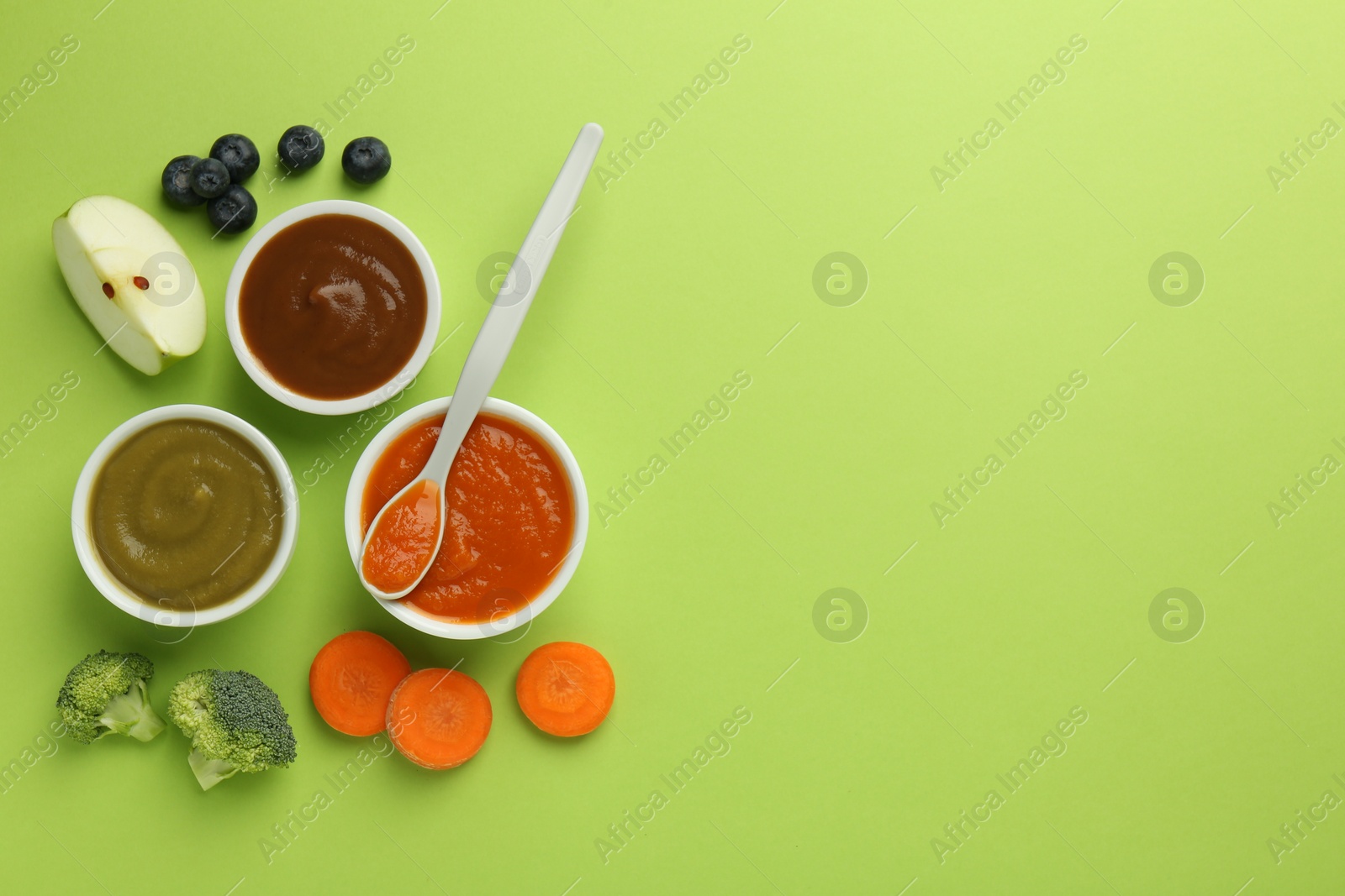 Photo of Bowls with healthy baby food, vegetables, fruits and spoon on light green background, flat lay. Space for text