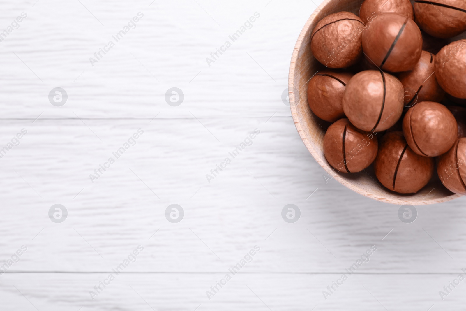 Photo of Delicious Macadamia nuts on white wooden table, top view. Space for text