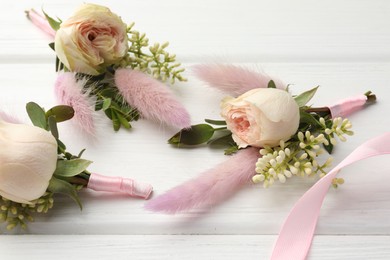 Photo of Small stylish boutonnieres and ribbon on white wooden table