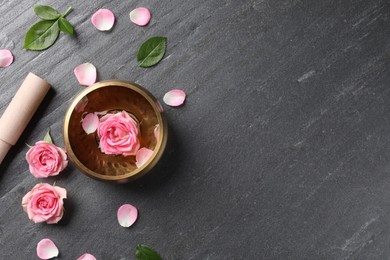 Photo of Tibetan singing bowl with water, beautiful rose flowers and mallet on gray table, flat lay. Space for text