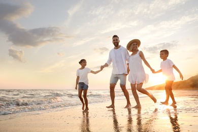 Photo of Happy family running on sandy beach near sea at sunset