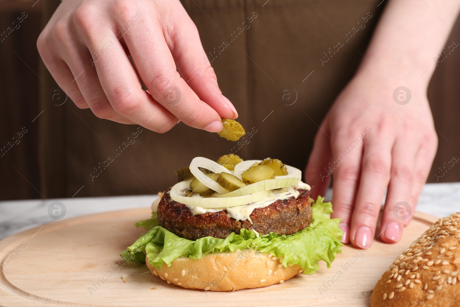 Photo of Woman making delicious vegetarian burger at table, closeup