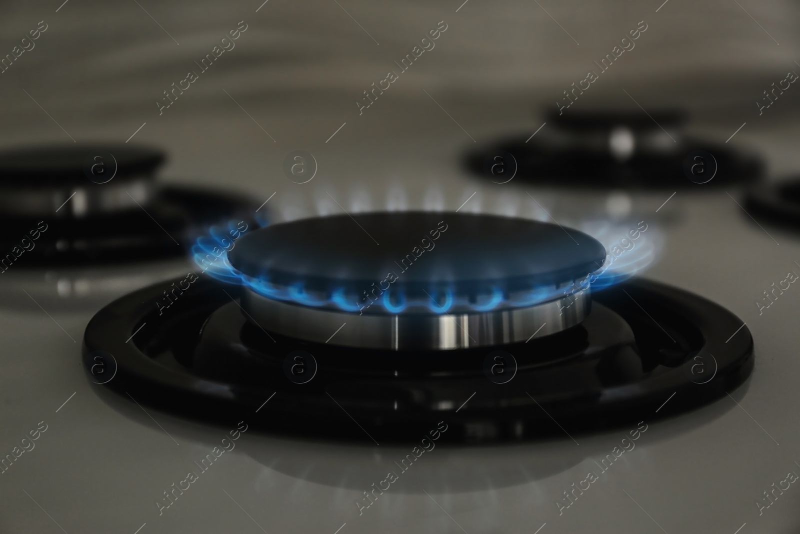 Photo of Gas burner with blue flame on modern stove, closeup