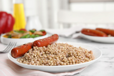 Tasty buckwheat porridge with sausages on table indoors