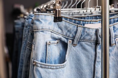 Photo of Hangers with stylish jeans on rack, closeup