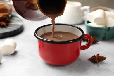 Photo of Pouring tasty hot chocolate into cup at light table, closeup