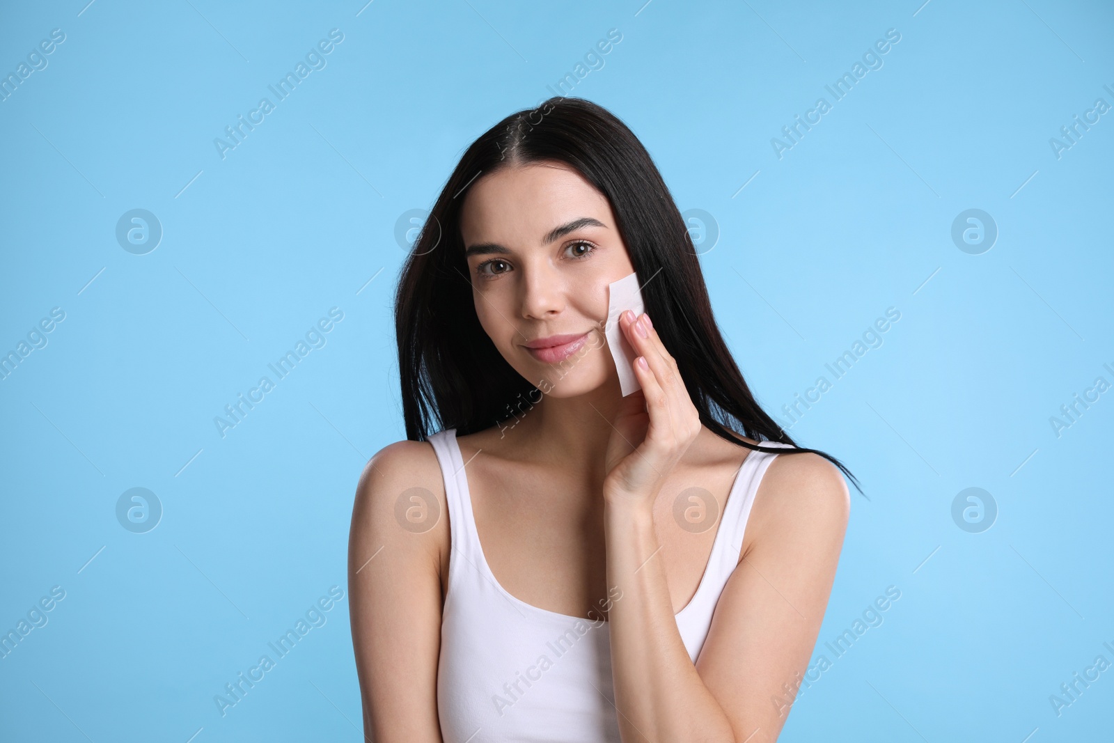 Photo of Beautiful woman using mattifying wipe on light blue background