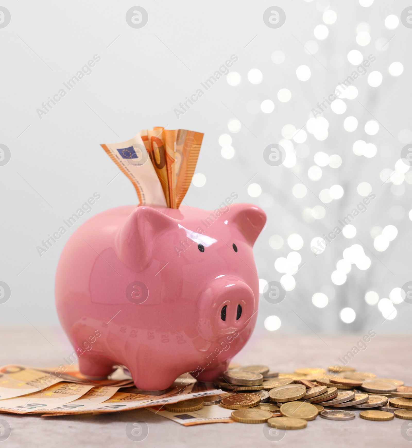 Piggy bank with euro banknotes and coins on grey table against blurred lights, space for text Photo of Piggy bank with euro banknotes and coins on grey table against blurred lights, space for text