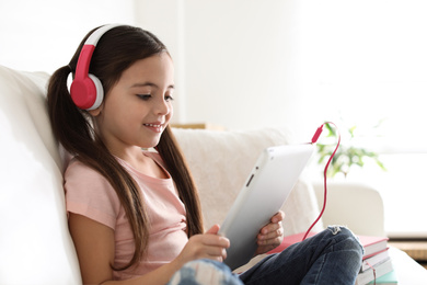 Cute little girl with headphones and tablet listening to audiobook at home