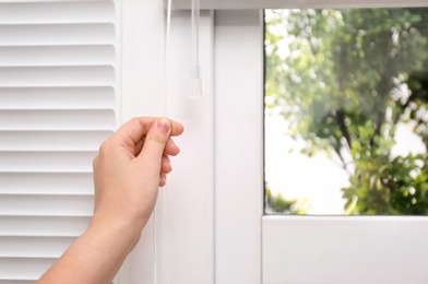 Photo of Woman opening white horizontal window blinds, closeup