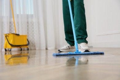 Photo of Professional janitor cleaning parquet floor with mop indoors, closeup. Space for text