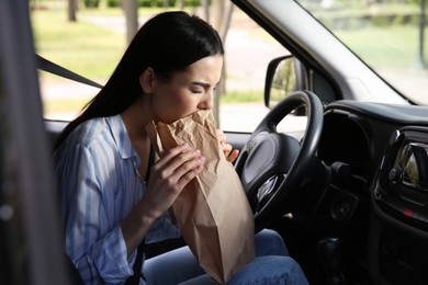 Photo of Young woman with paper bag suffering from nausea in car