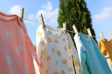 Photo of Clean baby onesies hanging on washing line outdoors. Drying clothes