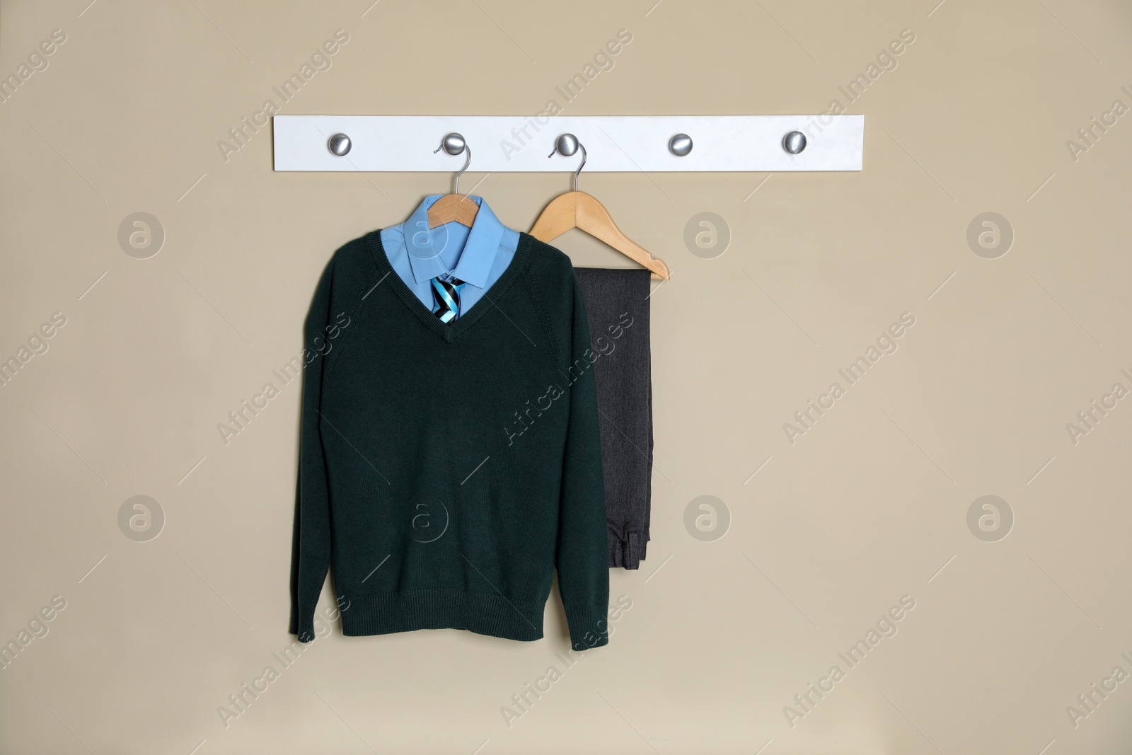 Photo of Shirt, jumper and pants hanging on beige wall. School uniform
