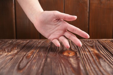 Photo of Woman holding hand above wooden table, closeup. Space for text