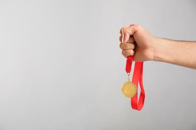 Photo of Man holding golden medal on grey background, closeup. Space for design