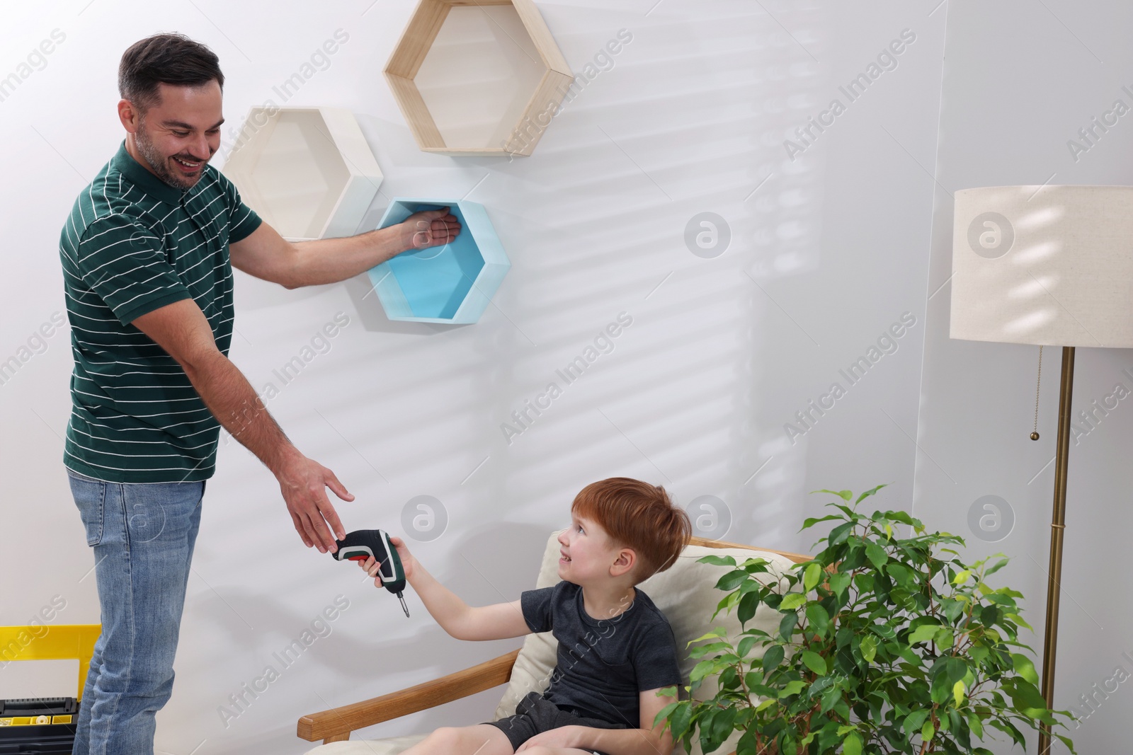Photo of Son giving tool to father at home. Repair work