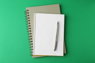 Photo of Notebooks and pen on green background, top view