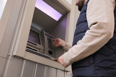 Photo of Man inserting credit card into cash machine outdoors, low angle view
