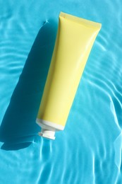 Tube with moisturizing cream in water on light blue background, top view