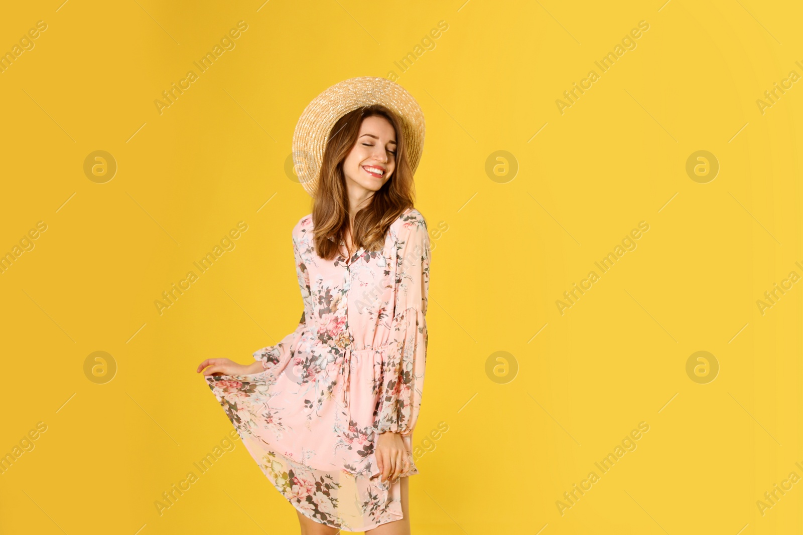 Photo of Young woman wearing floral print dress and straw hat on yellow background