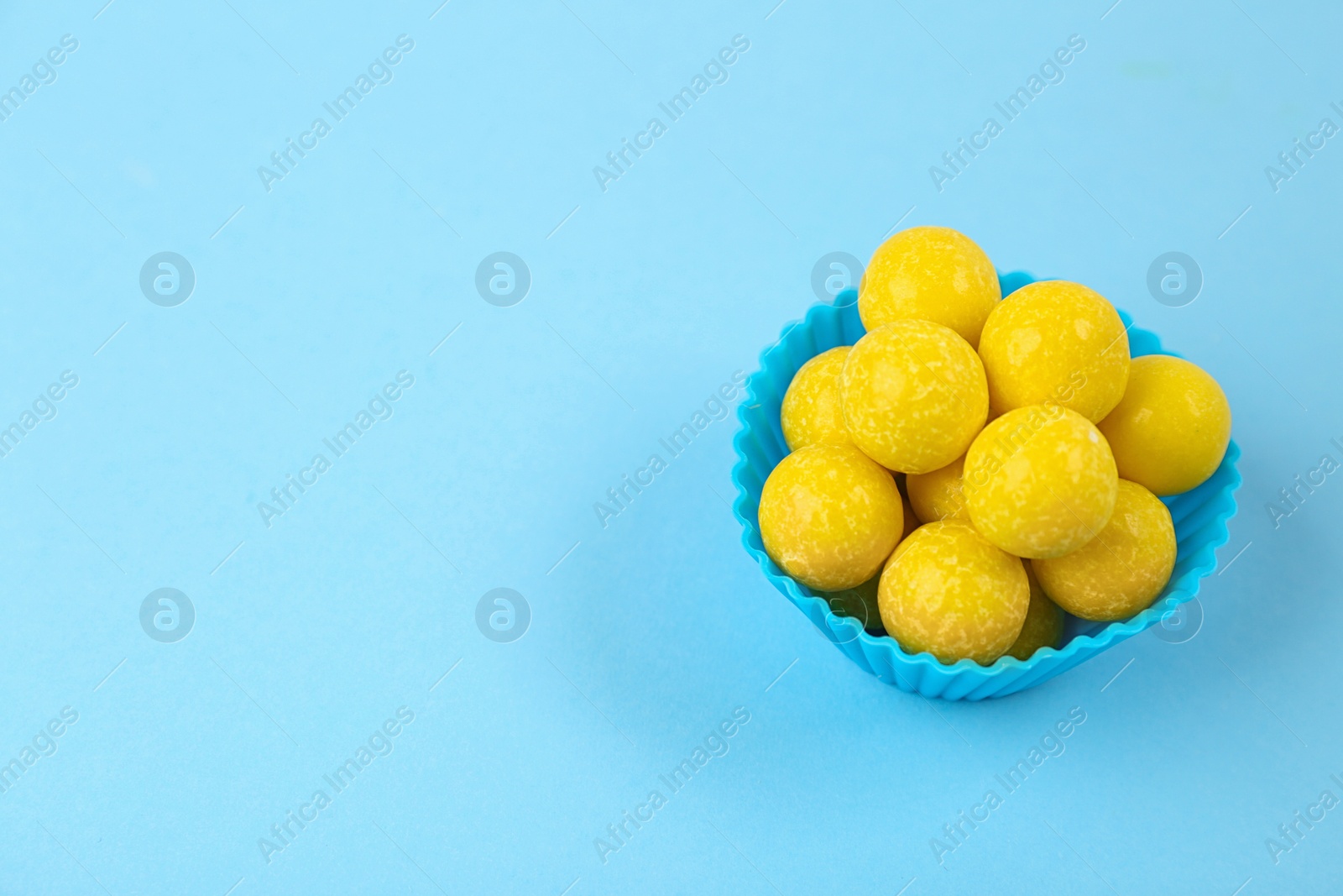 Photo of Delicious lemon chewing gums on light blue background. Space for text