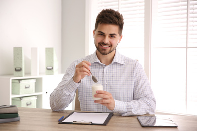 Photo of Happy young man with tasty yogurt in office