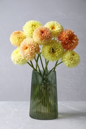 Photo of Beautiful yellow dahlia flowers in vase on table against grey background